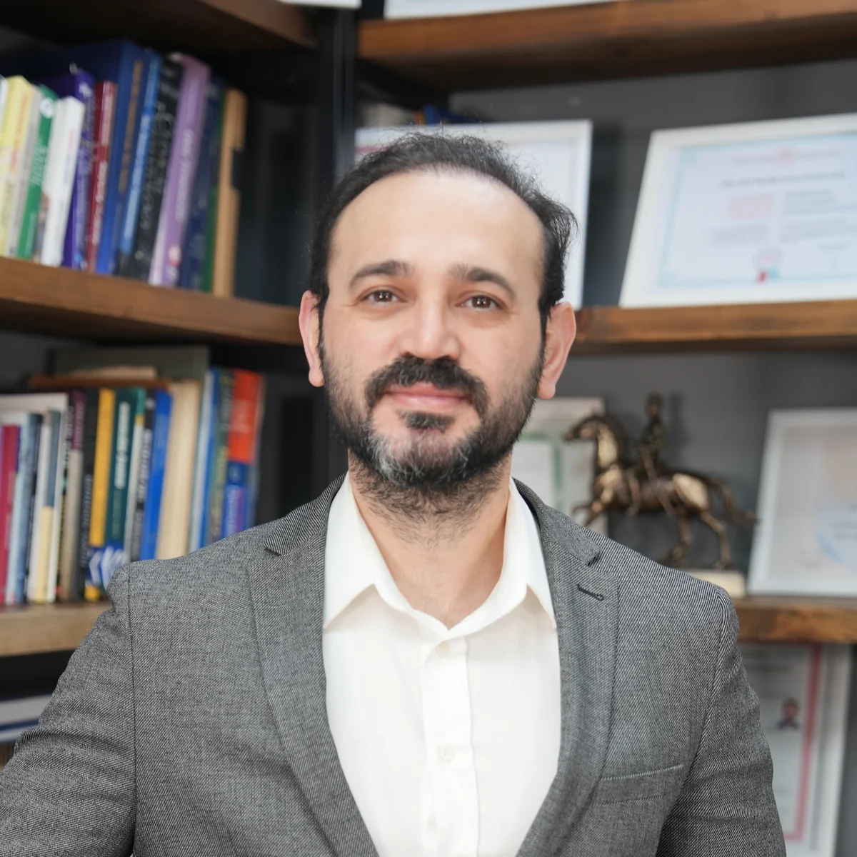 Porträt von Akif Mehmetoğlu in grauem Sakko und weißem Hemd vor einem Bücherregal