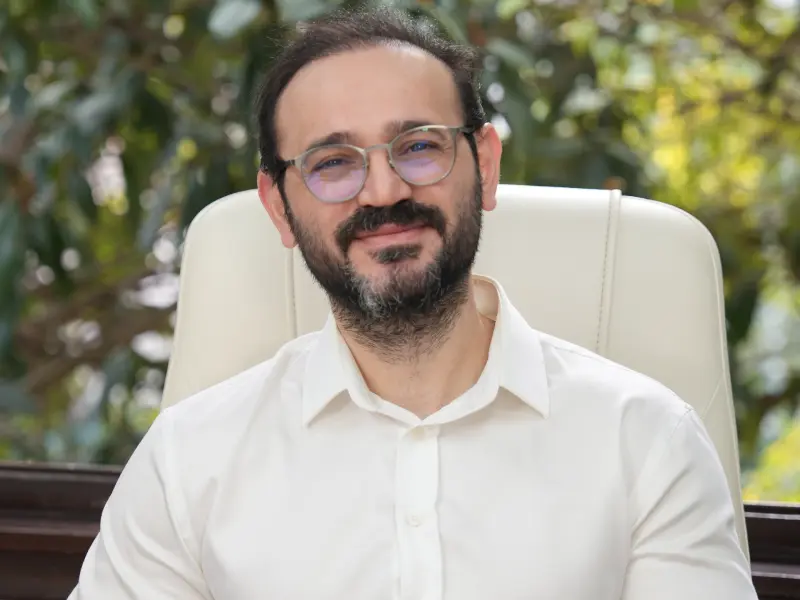 Portrait of Dr. Akif Mehmetoğlu smiling in a white shirt and glasses, inviting international patients to schedule a free virtual consultation for facial plastic surgery or hair transplant assessment.
