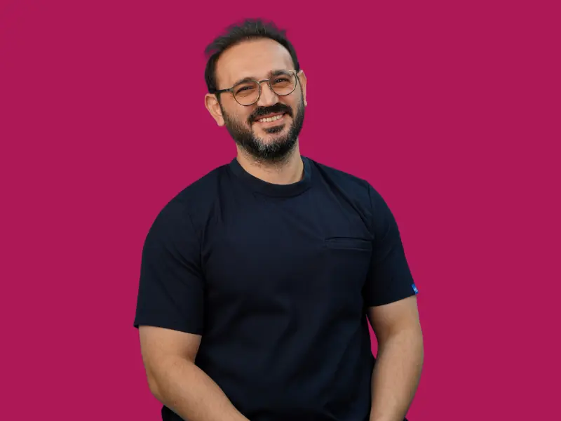 Porträt von Akif Mehmetoğlu mit Brille in dunkelblauer OP-Kleidung vor magentafarbenem Hintergrund
