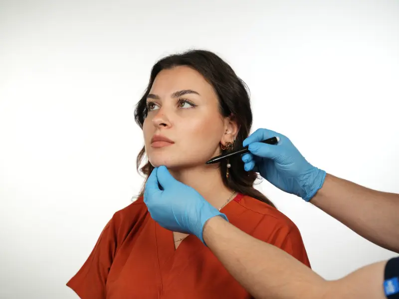 Clinician in blue gloves marking a woman’s jawline with a pen during pre-operative facial planning.