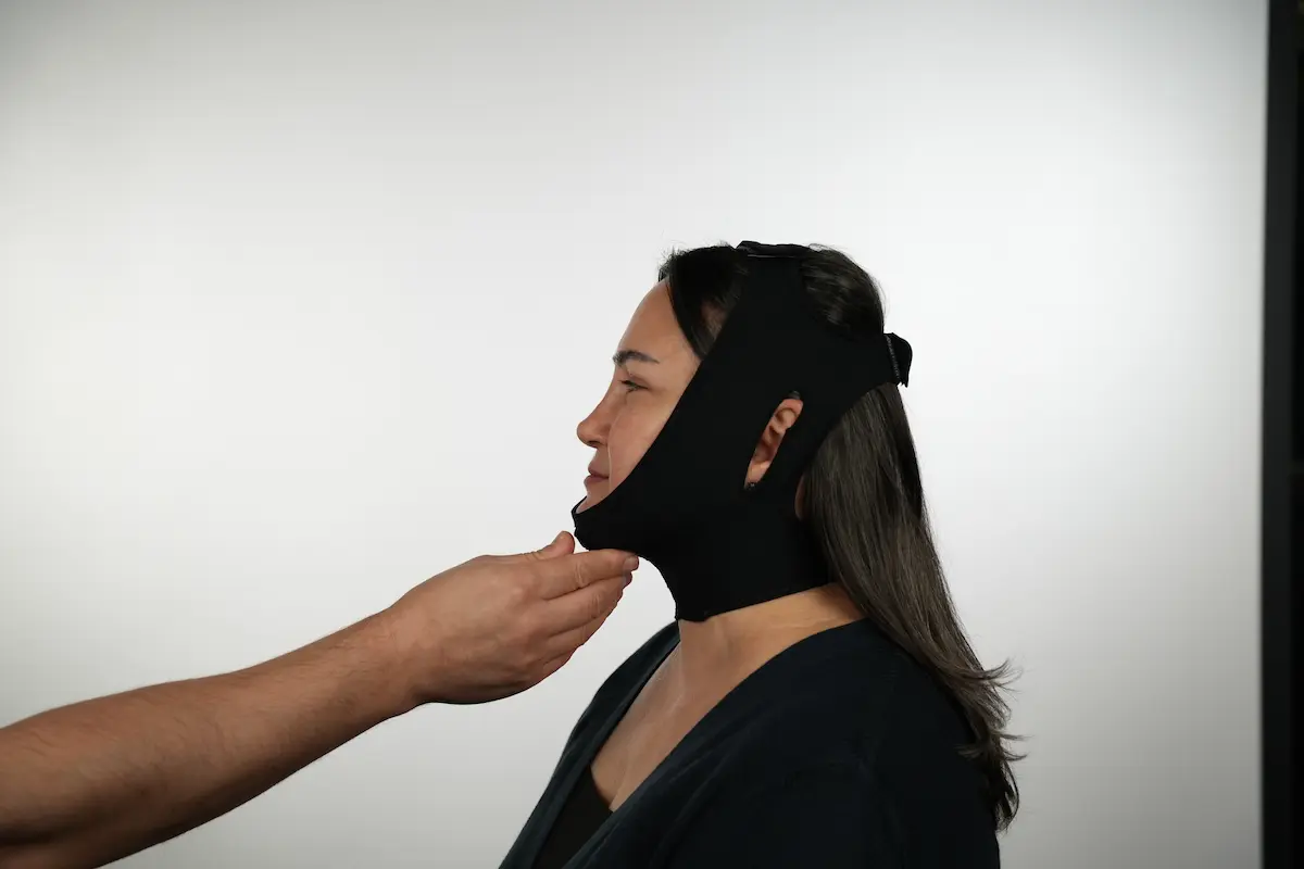 Patient wearing a black chin and neck compression garment being adjusted by a clinician.