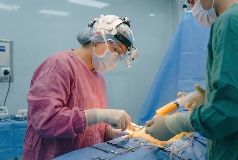 A plastic surgeon in full protective gear performing surgery with an assistant in a modern operating room, illustrating hospital standards when asking “Is It Safe to Have Plastic Surgery in Turkey?”.