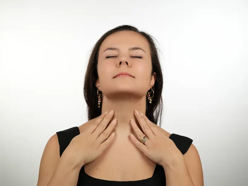 Woman touching the front of her neck with both hands, illustrating concern about neck skin laxity or aging.