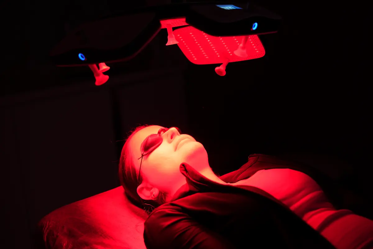 Patient wearing protective goggles under red light therapy devices during a recovery session.