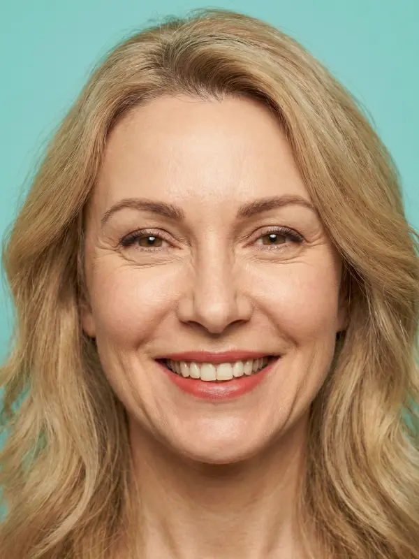 Symbolbild zu SMAS-Facelift und Halsstraffung: lächelnde Frau mit langem blondem Haar vor türkisfarbenem Hintergrund