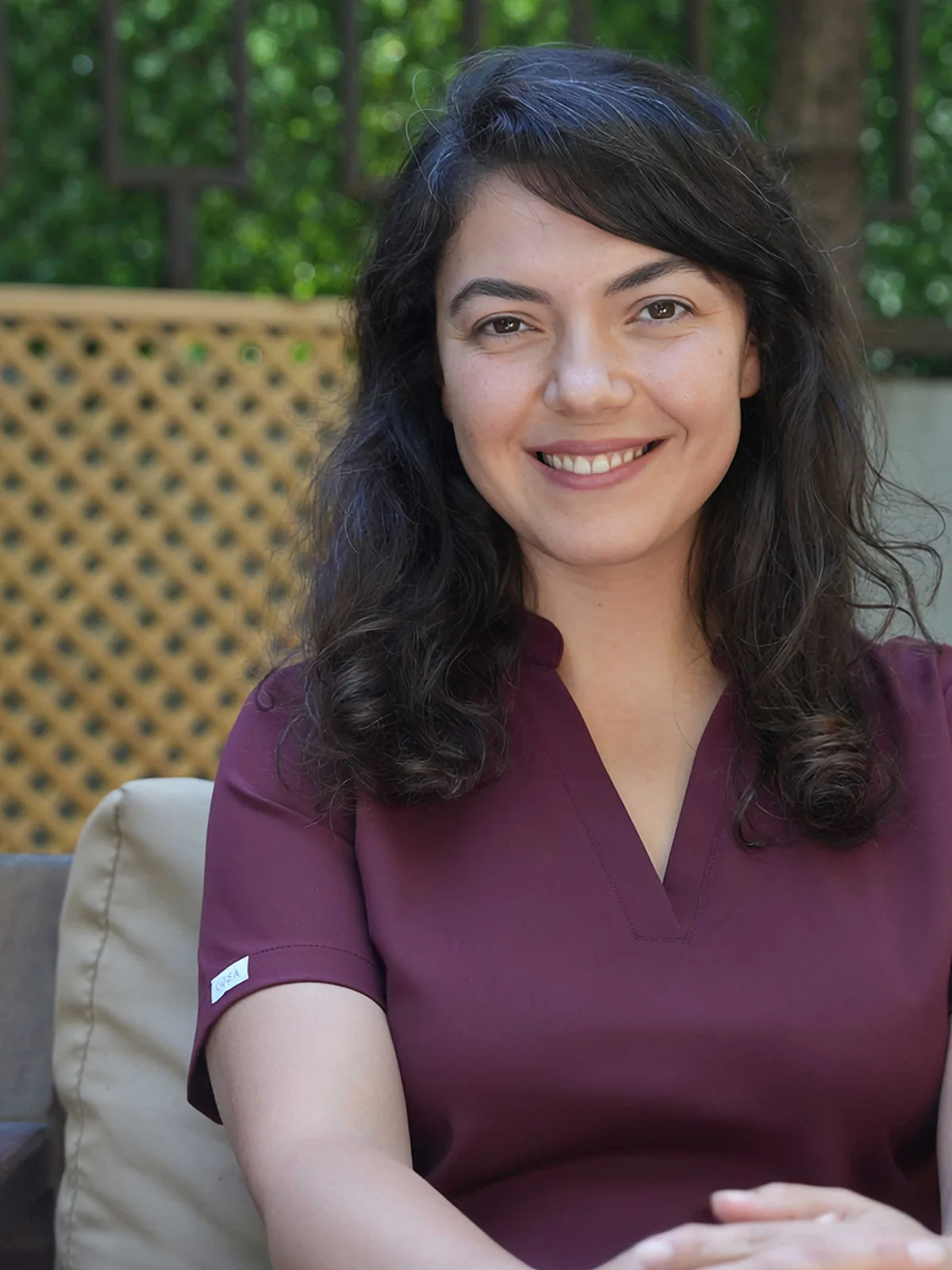 Aylin Akbulut Yılmaz in bordeauxroter OP-Kleidung sitzt lächelnd auf einer begrünten Terrasse