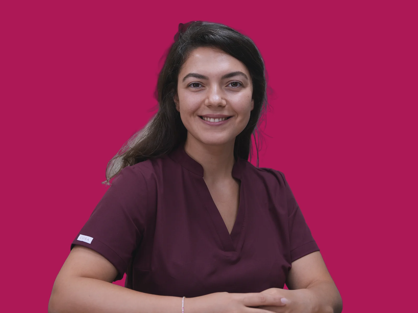 Porträt von Aylin Akbulut Yılmaz in bordeauxroter OP-Kleidung vor magentafarbenem Hintergrund